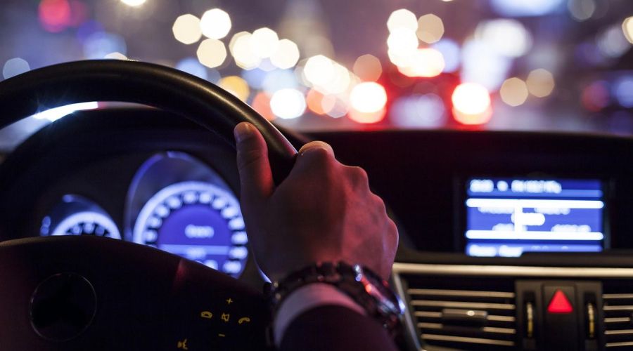 A man driving with city nightlife outside the windshield.