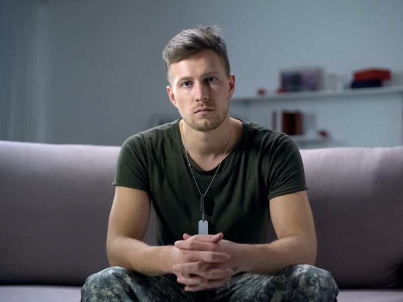 Military serviceman in fatigues, sitting on a sofa with hands clasped.